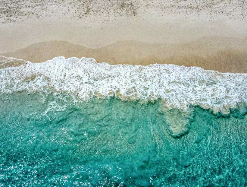 Luftaufnahme der türkisfarbenen Brandung an einem Sandstrand der Seychellen.