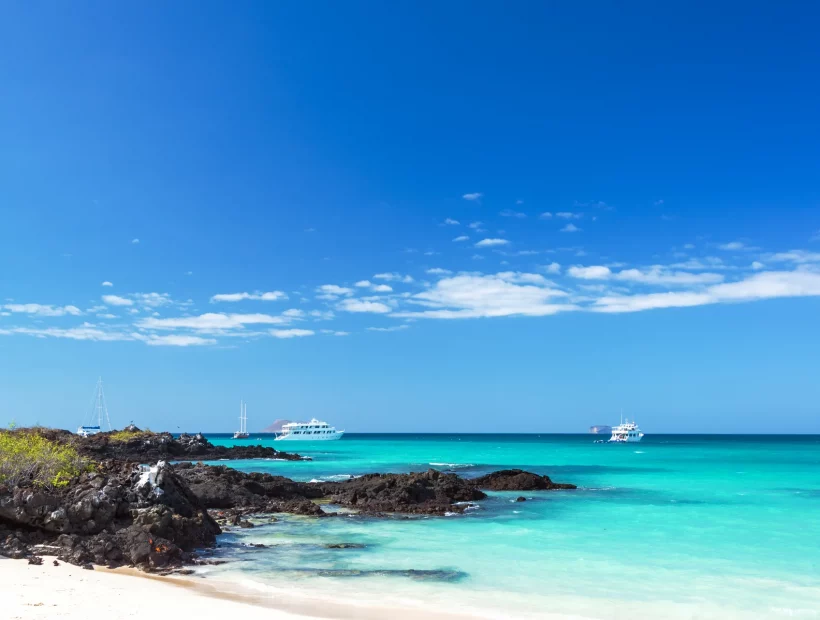 Galápagos-Strand mit türkisfarbenem Meer und Expeditionsschiffen vor der Küste Santa Cruz